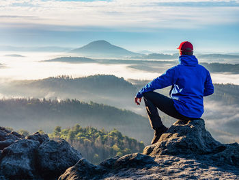 Man on the peak of rock. man sit with hand on knee with beautiful sunrise landscape. hiker is watch