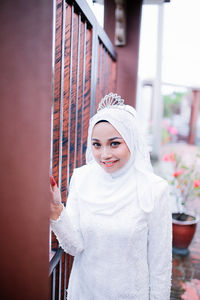 Portrait of smiling young woman standing by gate