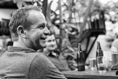 Smiling man looking away while sitting outdoors with friend