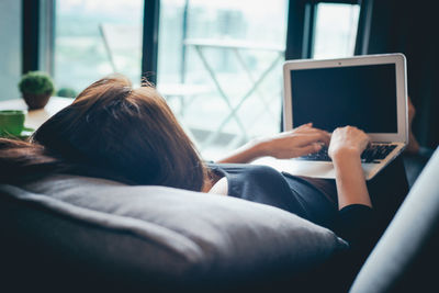 Rear view of woman using mobile phone at home