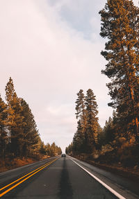 Empty road amidst trees against sky during autumn