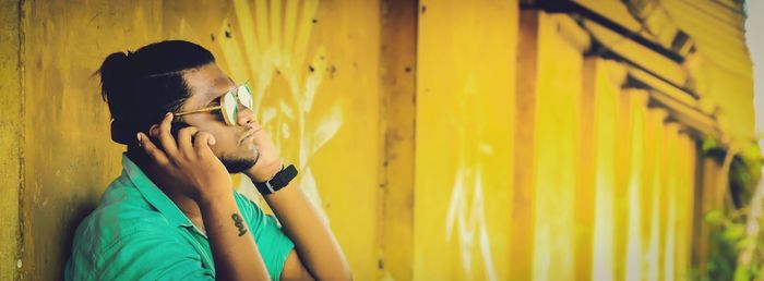 Young man listening music against yellow wall