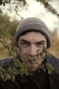 Close-up portrait of young man wearing hat by branch