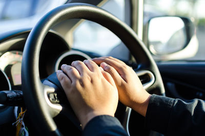 Cropped hands driving car in sunny day