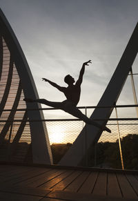 Silhouette man jumping at sea against sky during sunset