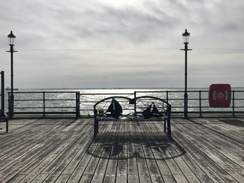 Rear view of people sitting on pier at sea against sky
