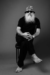 Full length of man sitting on chair against gray background