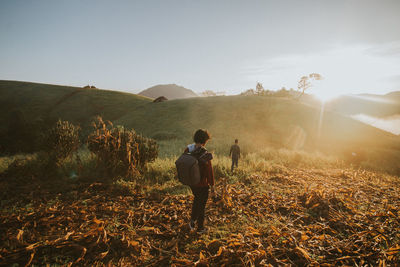 Rear view of people walking on field during sunset