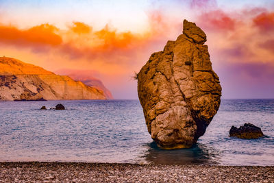 Rock formation on sea shore against sky during sunset