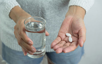 Midsection of woman holding medicine and drinking water at home