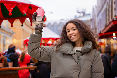 Portrait of young woman with arms raised standing in city