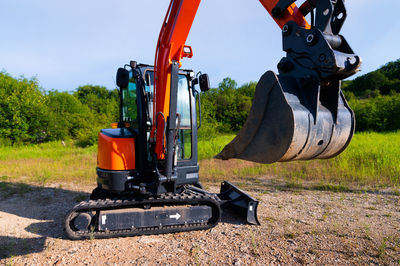 Bulldozer stands on a piece of land against the backdrop of a bright blue sky and green trees