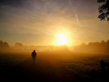 Rear view of man on field against sky during foggy weather