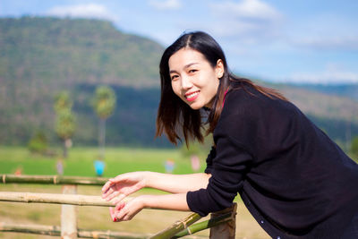 Portrait of smiling young woman standing against railing