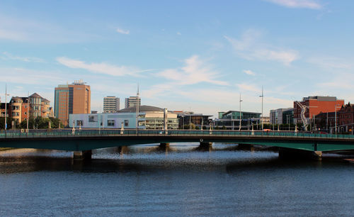 Bridge over river by buildings in belfast city against sky