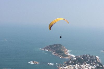 Person paragliding over sea against sky