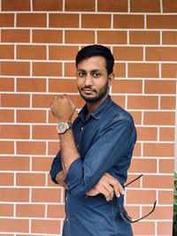 Portrait of young man standing against brick wall