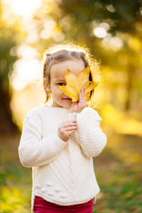 Portrait of girl holding leaf over face while standing on land