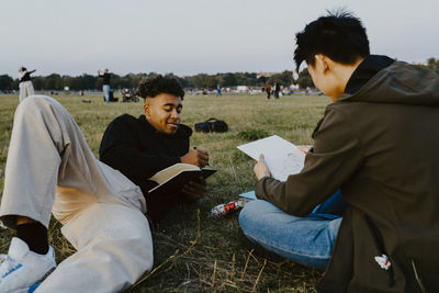 Male friends drawing in book at park during sunset