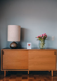 Vintage sideboard forniture with old lamp, potted flowers in a vase, gift card with a read heart.