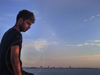Young man standing by sea against sky during sunset