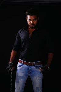 Portrait of young man standing against black background