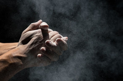 Cropped image of hand with powder against black background