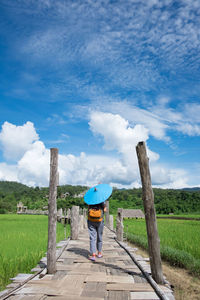 Rear view of woman walking on boardwalk over field against sky