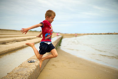 Full length of boy jumping at beach against sky