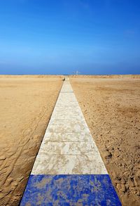 Diminishing perspective of footpath on beach against blue sky