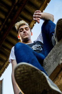 Low angle portrait of teenage boy sitting on retaining wall