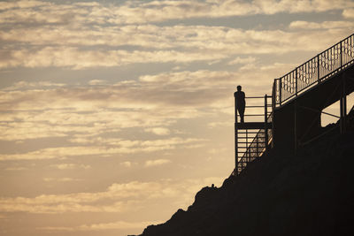 Silhouette man standing by railing against sky during sunset