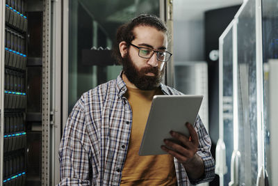 Technician wearing eyeglasses looking at tablet pc in server room