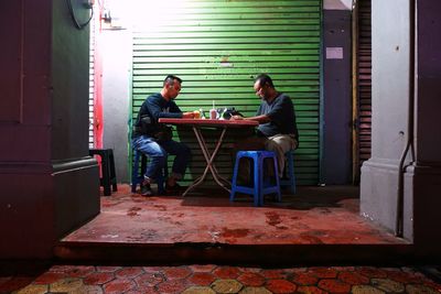 Male friends sitting at table by shutter during night