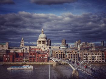 Boat moving under millennium bridge by st paul cathedral against cloudy sky