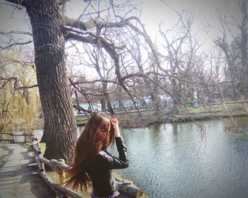Young woman sitting on tree trunk by lake against sky