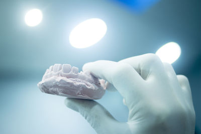 Cropped hand of person holding dental mold against illuminated lights