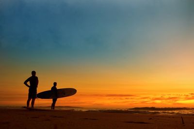 Silhouette people on beach against sky during sunset