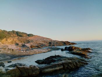 Rocky seashore against clear sky during sunset