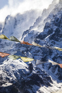 Rows of colorful buddhist prayer flags hanging on ropes on background of rocky himalayas covered with snow in winter in nepal