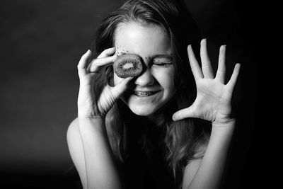 Close-up of smiling young woman with kiwi gesturing against black background