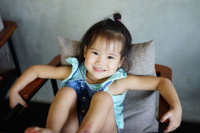 Portrait of girl smiling while sitting on chair at home