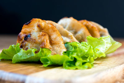 Close-up of fresh dumplings served with lettuce on cutting board against black background