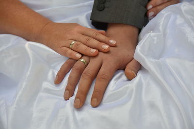 Cropped hands of couple wearing rings on white textile