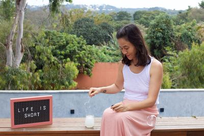 Young woman sitting on table against trees