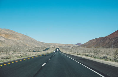 Empty road by mountains against clear blue sky