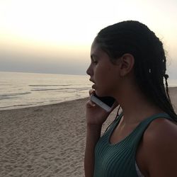 Portrait of young woman looking away at beach against sky
