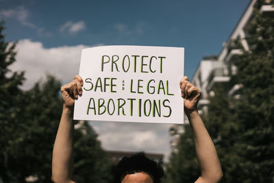 Cropped hand of woman holding text against sky