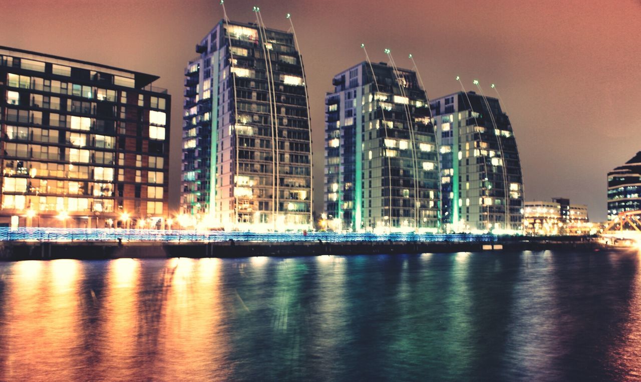 architecture, building exterior, built structure, waterfront, illuminated, city, water, reflection, night, river, building, modern, sky, office building, skyscraper, cityscape, residential building, tower, residential structure, tall - high