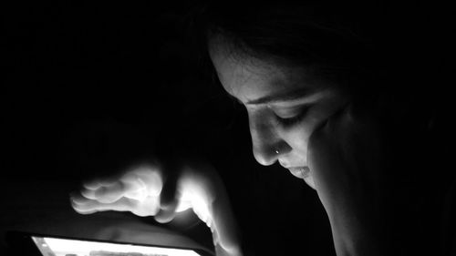 Close-up portrait of young woman using smart phone in darkroom